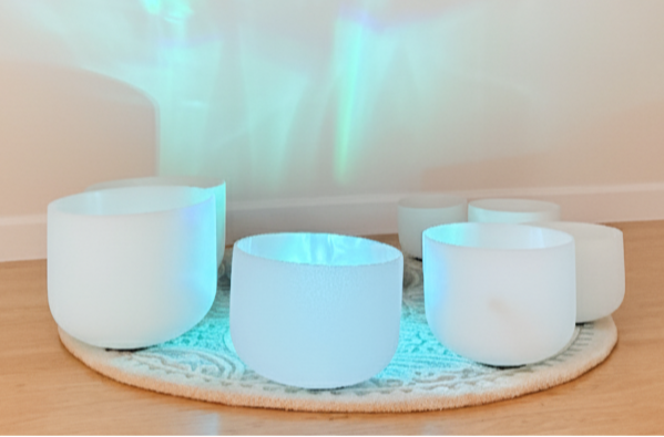 White ceramic bowls on a wooden floor with decorative wall patterns and a plant.