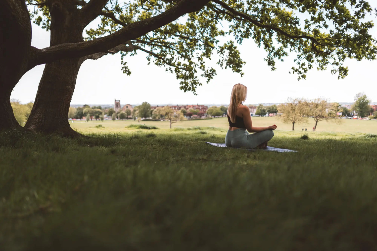 a girl gracefully performing a yoga pose under a large, shady tree, surrounded by a tranquil natural setting with soft sunlight filtering through the leaves